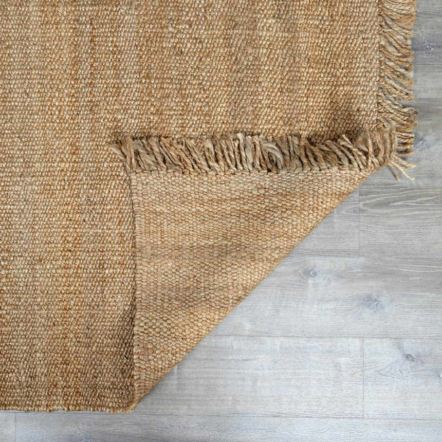 Close-up of the natural beige Oaks Perfect Flatweave Jute Rug showing texture and fringe detail on light gray wood floor. Fold