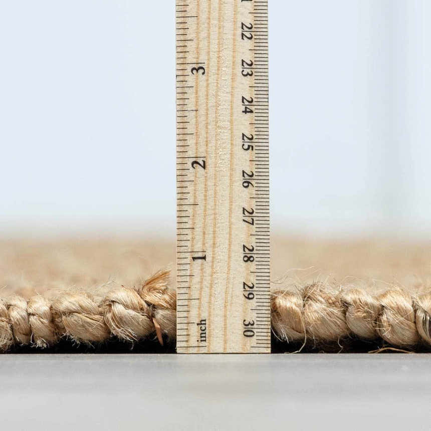 Close-up of the texture and thickness of the beige Oaks Perfect Flatweave Jute Rug, with a ruler showing the pile height. Pile