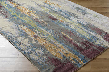 Close-up of the Kabugao Handmade Wool Rug showing its blue, charcoal, and peach abstract design on wood floors. Corner