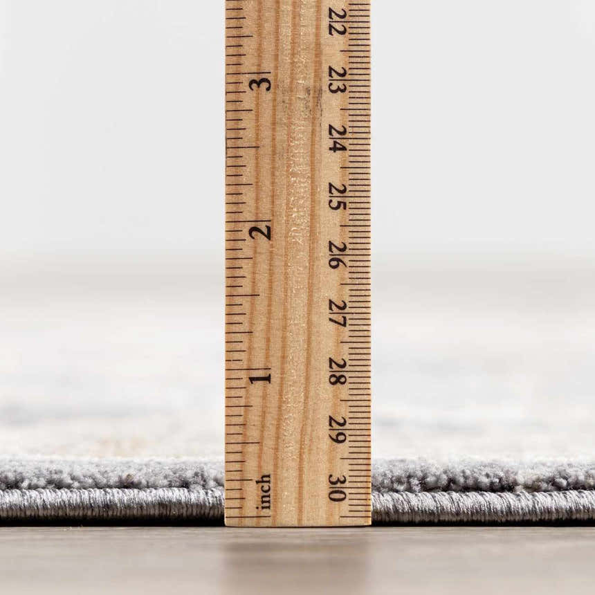 Close-up of the Kanimbla rug's thickness, showing its plush pile height with a ruler. Gray and beige tones. Pile