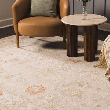 Living room scene with beige Kitchener Oushak Thick Luxe Area Rug, tan leather chair, and round side table. Roomscene-Rectangle