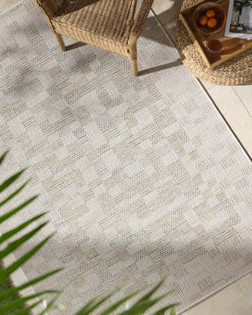 Arshad Ivory Area Rug in a bright sunroom with wicker chair and ottoman. Beige, ivory, and tan tones. Roomscene-Rectangle