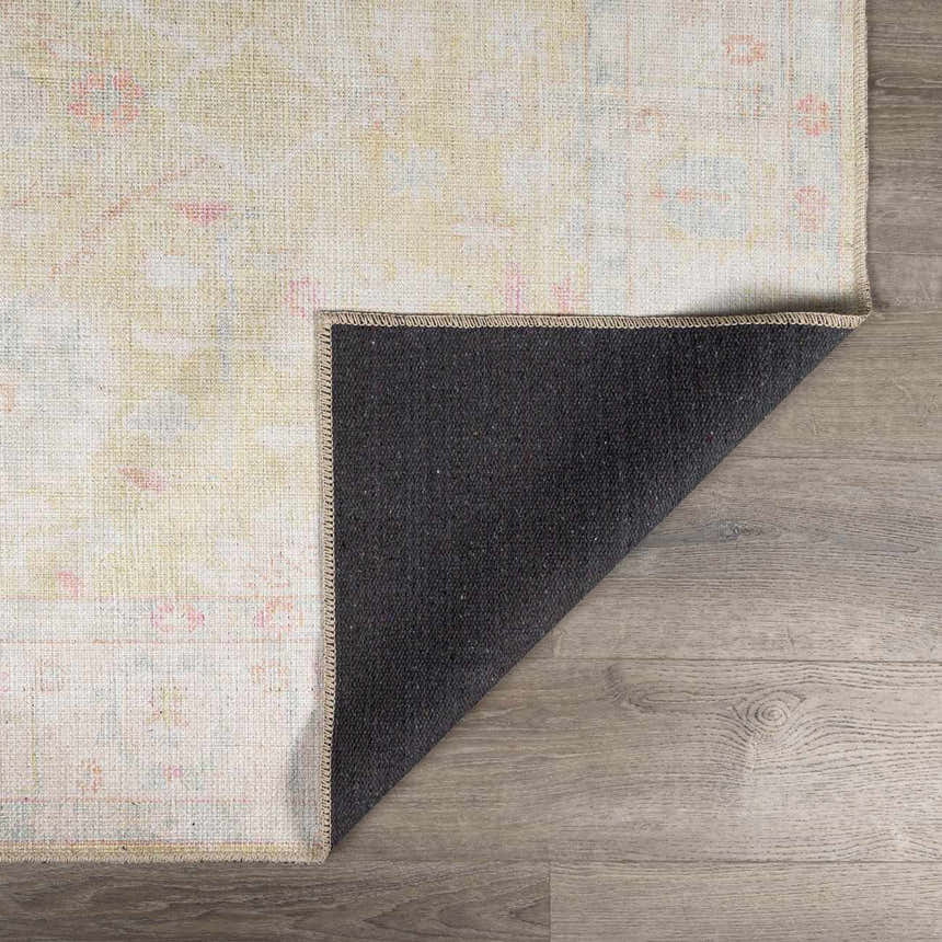 Close-up of the Bozkurt Boutique Washable Rug showing its cloud gray, pink, and yellow vintage-style pattern and dark gray backing. Fold