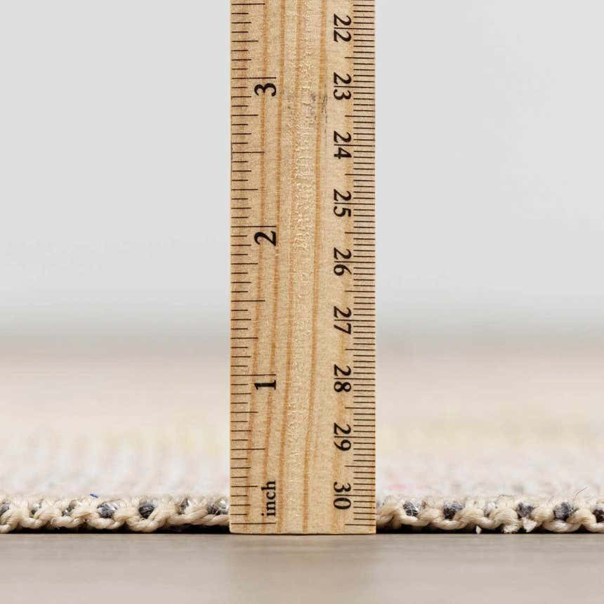 Close-up of the Bozkurt Boutique Washable Rug showing the rug's thickness with a ruler. Cloud Gray and Lambswool colors. Pile
