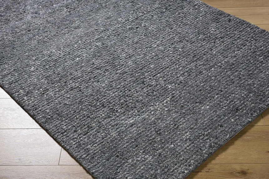 Close-up of the Winta Black Wool Area Rug. Hand-tufted rug in shades of gray with a textured, nubby design on wood floor. Corner