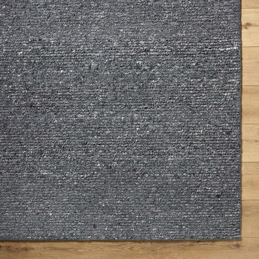 Close-up of the hand-tufted Winta Black Wool Area Rug, showing its gray tones and nubby texture on a light wood floor. Corner