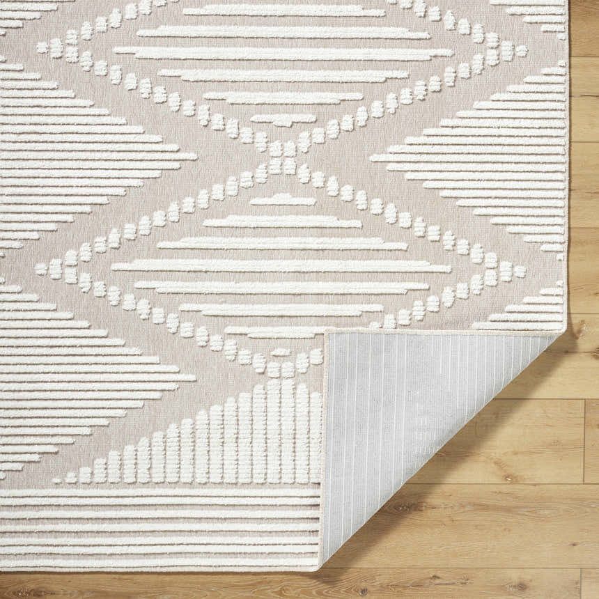 Close-up of the Annika Washable Area Rug. Off-white and tan rug features a geometric diamond pattern and a textured, machine-woven design. Fold
