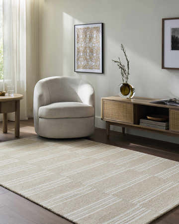 Living room scene with beige Argyro Area Rug, ivory chair, and sandstone-toned furniture. Warm, transitional style. Roomscene-Rectangle
