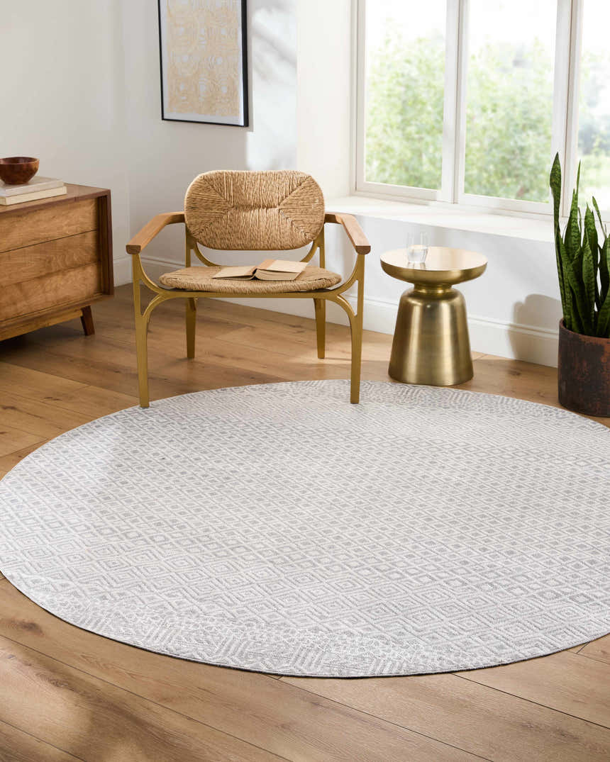 Sunlit room with round Maanas Washable Area Rug in gray, woven chair, wood floors, and modern decor. Roomscene-Round
