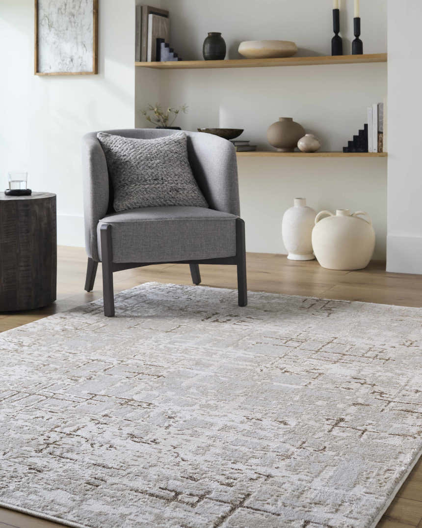 Living room scene with a gray chair on the Auriel Beige Area Rug. The rug has a contemporary design with beige, cream, and tan colors. Roomscene-Rectangle