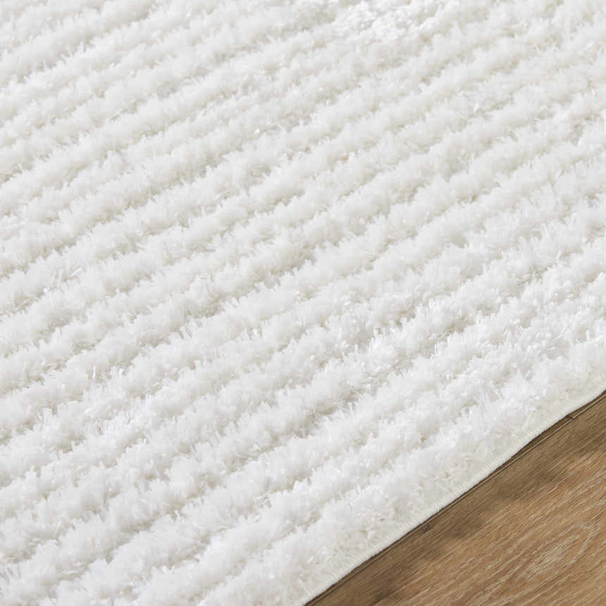 Close-up of the white Alysha Area Rug, a soft shag rug with a subtle striped pattern on a wood floor. Texture