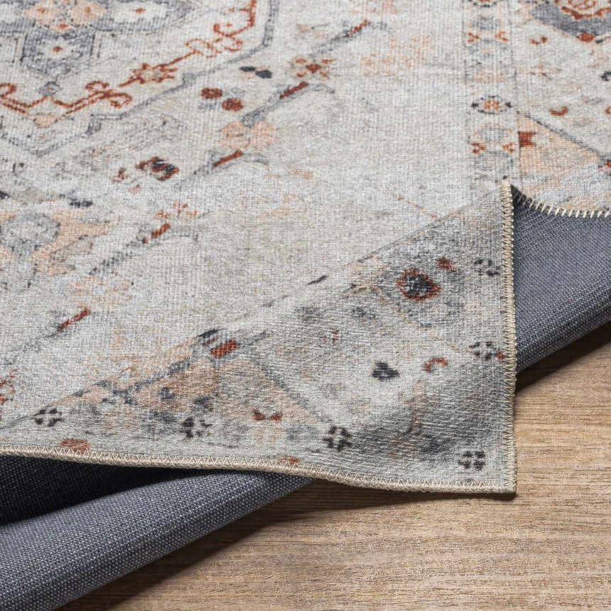 Close-up of the Midtown Washable Area Rug. Features a traditional oriental pattern in brick red, charcoal, gray, and peach tones. Fold