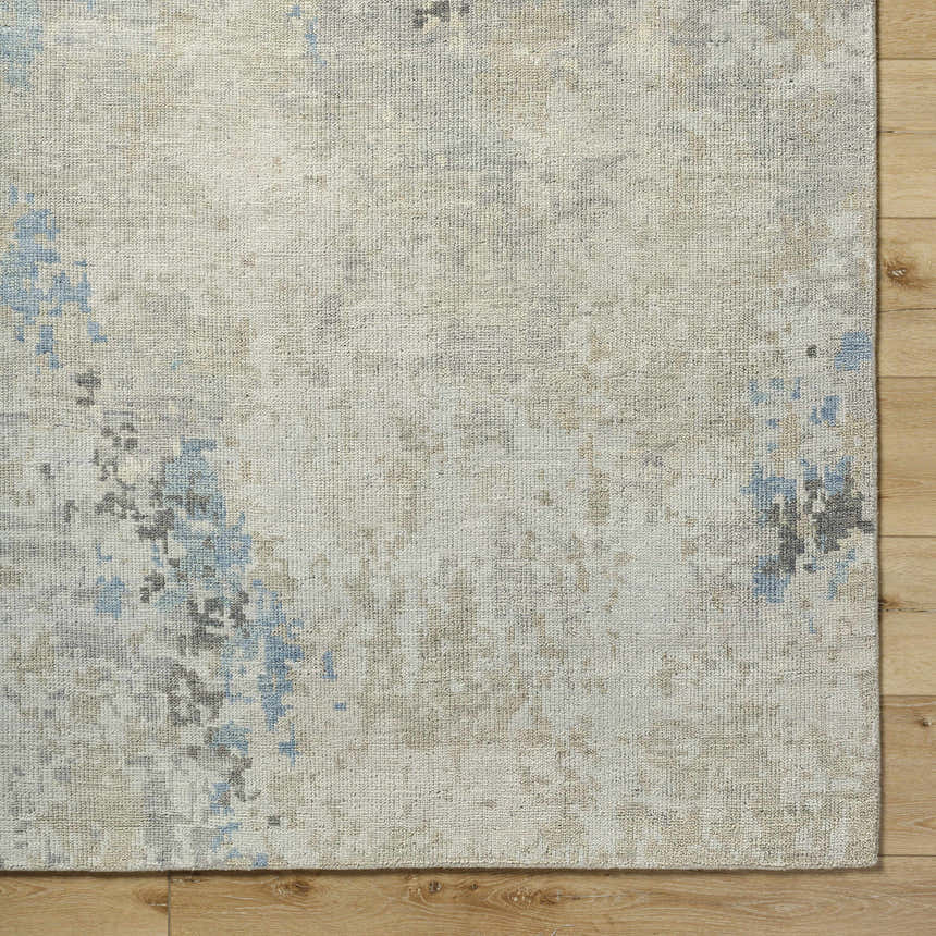 Close-up of the Marco Handmade Wool Rug. Features charcoal, cream, denim, and beige tones with a subtle contemporary pattern. Corner