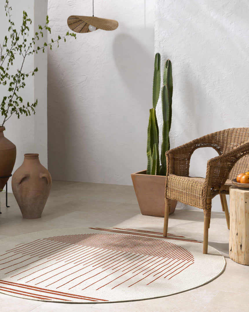Minimalist room with a round Nabil Cream Area Rug, wicker chair, terracotta pots, and cactus. Roomscene-Round
