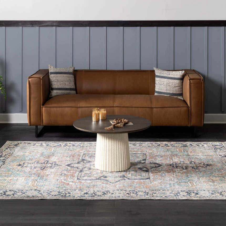 Living room scene with a brown leather sofa and Green Nisa Tumble Dry Washable Rug in pale blue, orange, and navy. Roomscene-Rectangle