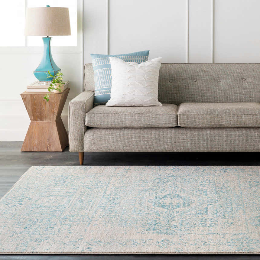 Living room scene with light beige Omega Area Rug, gray sofa, teal lamp, and wood side table. Roomscene-Rectangle