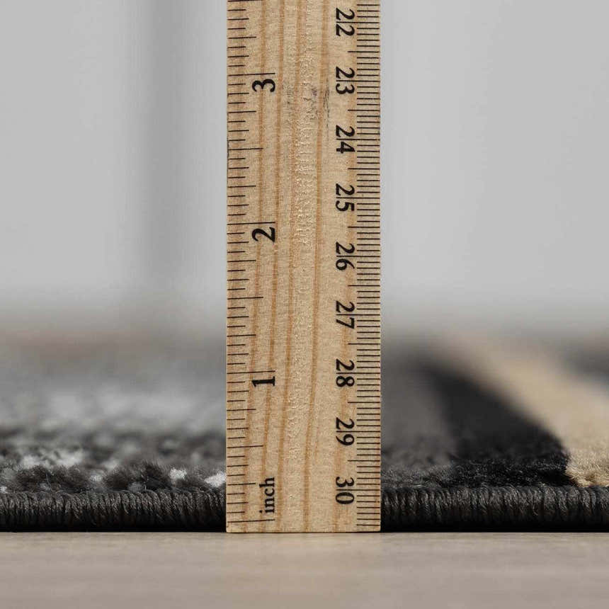 Close-up of the pile height of the Buckhaven Area Rug, showing black, gray and beige tones with a ruler. Pile