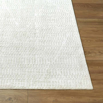 Close-up of the Pabla Cream Area Rug showing its ivory color and subtle geometric pattern on wood flooring. Front