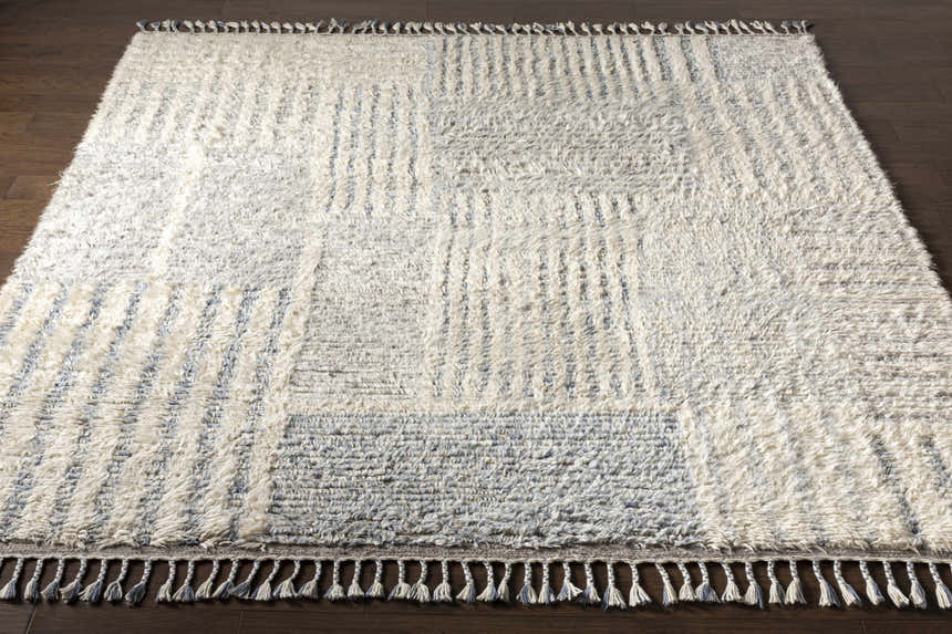 Close-up of the hand-knotted Plean Premium Rug, a 100% wool rug in cream and denim with a geometric pattern and tassels. Front