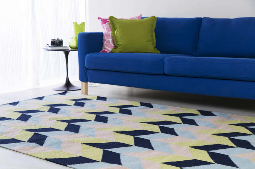 Living room scene with a blue sofa and Pojoaque Area Carpet in dark blue, pink, and olive geometric pattern. Roomscene-Rectangle