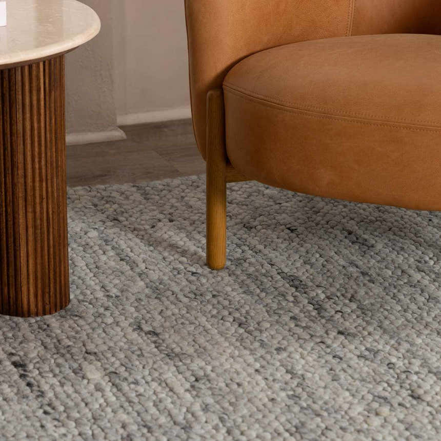 Close-up of the Olisa Gray Wool Area Rug, showing its looped texture and light gray and natural gray tones, styled with a chair. Roomscene-Rectangle