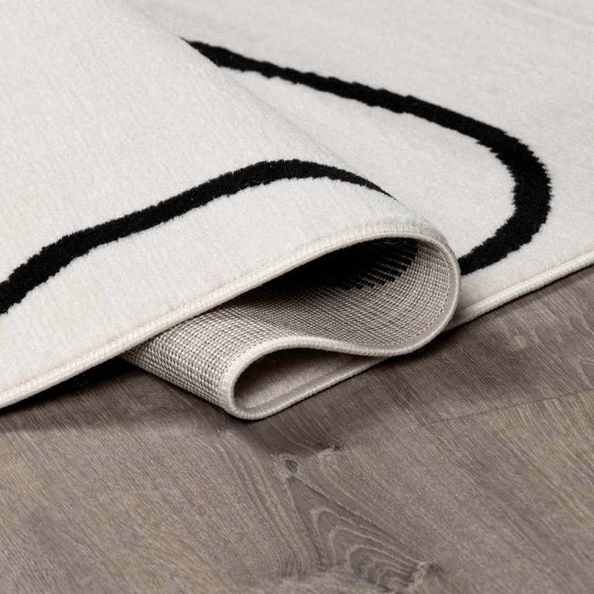Close-up of the Eilir Modern Low Profile Boho Rug showing its bone color and black abstract line design. Fold