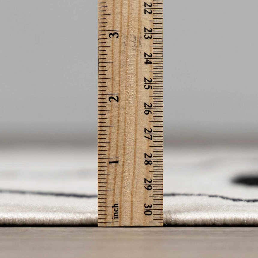 Close-up of the low pile height of the Eilir Modern Boho Rug in bone and black with a ruler for scale. Pile