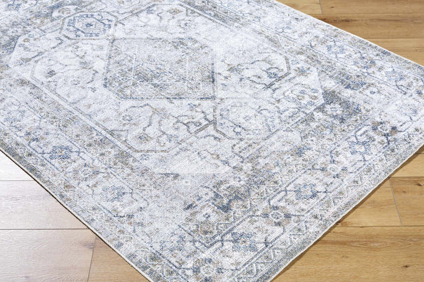 Close-up of the Annlea Washable Area Rug. Farmhouse style rug with blue, sage, and white traditional pattern detail. Corner