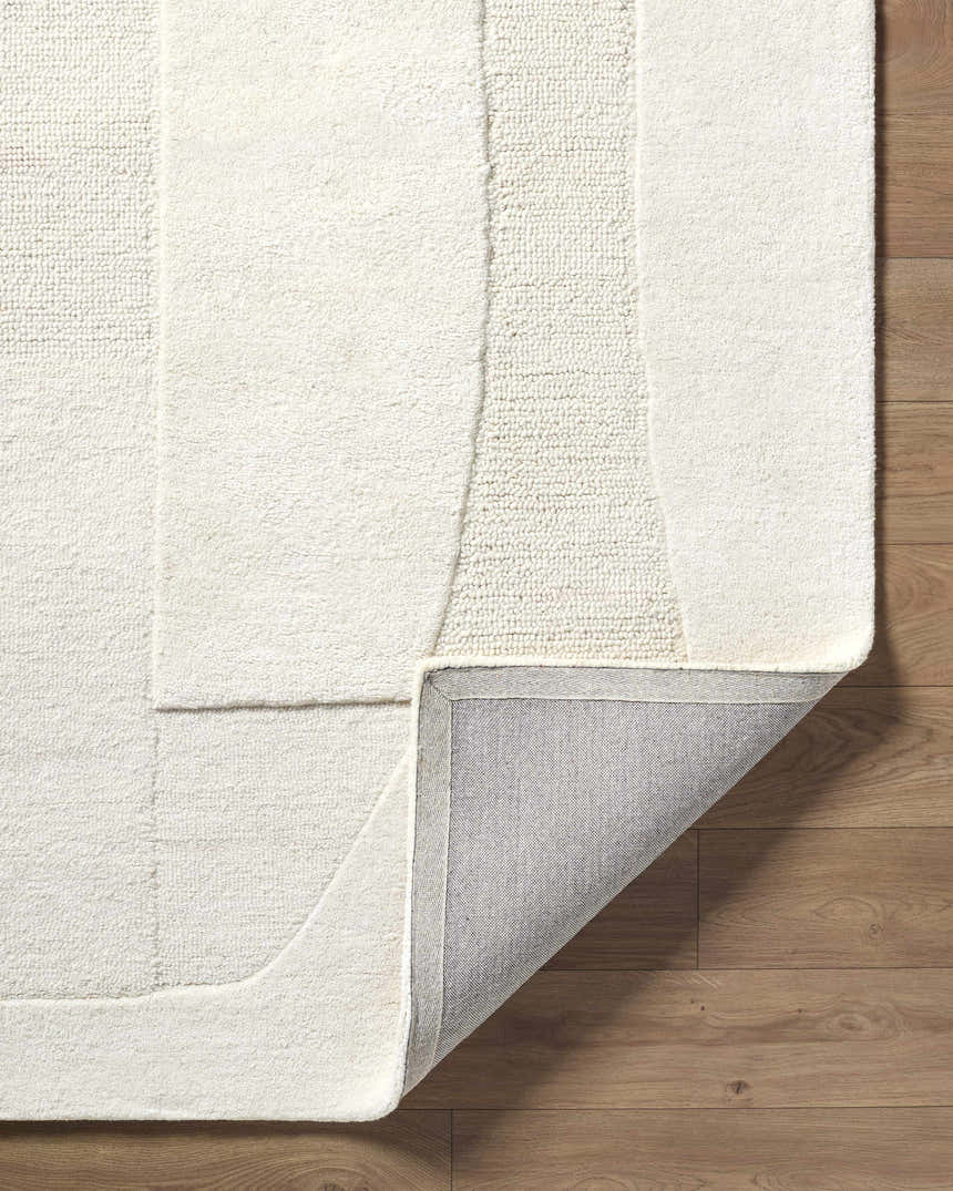 Close-up of the Agneza Area Rug showing the ivory wool texture, geometric pattern, and backing on wood floor. Fold