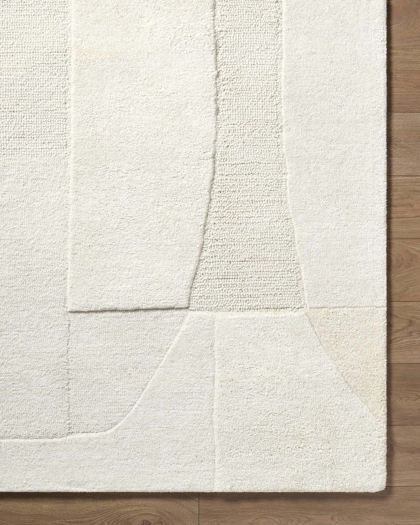 Close-up of the Agneza Area Rug, a hand-tufted wool rug with a geometric design in beige, cream, ivory, and tan. Corner