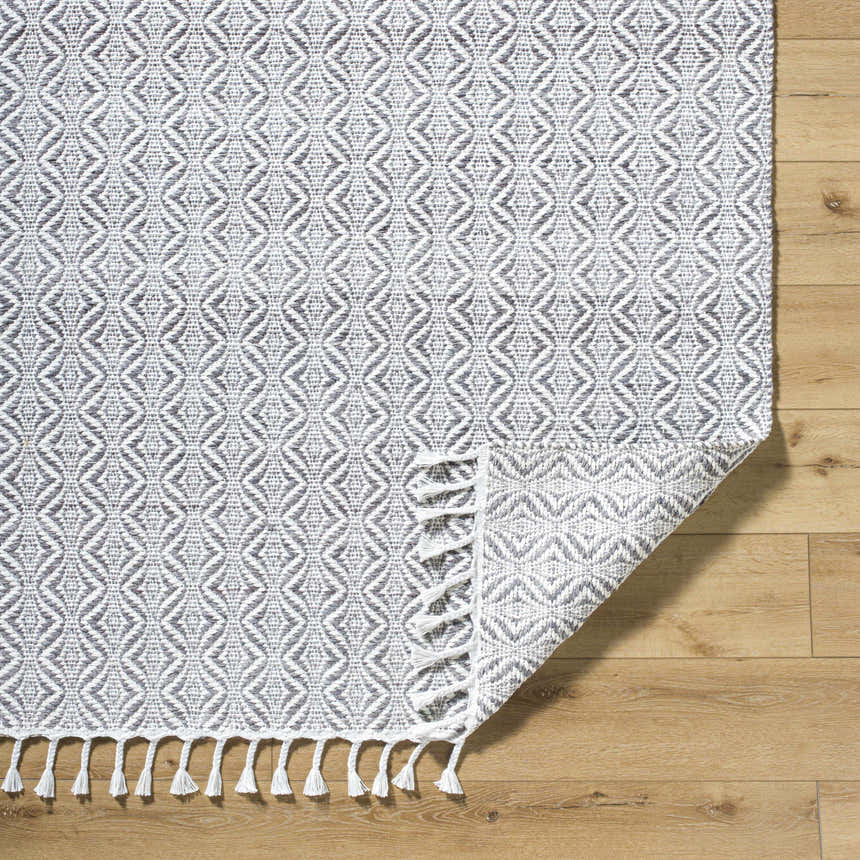 Close-up of the Anelia Medium Gray Area Rug. Hand woven recycled PET yarn with dove gray and ivory diamond pattern and white tassels. Fold
