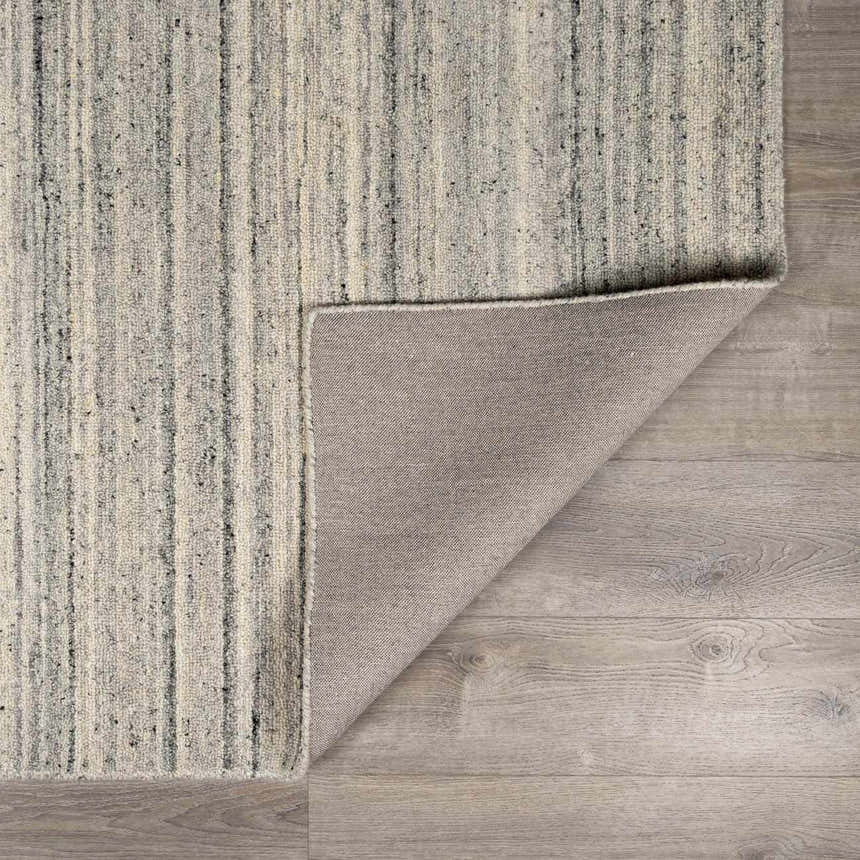 Close-up of the hand-tufted Capote Charcoal Area Rug. Wool rug with vertical charcoal, ivory, and slate gray stripes. Fold