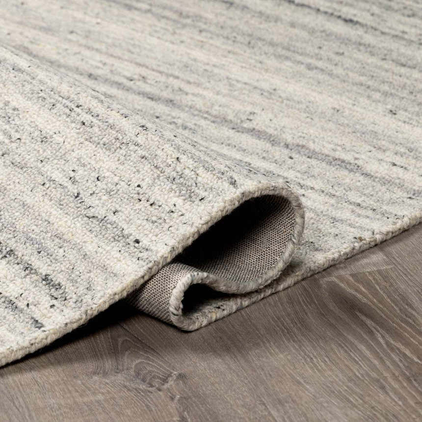 Close-up of the hand-tufted Capote Charcoal Area Rug showing its ivory, slate gray, and charcoal wool texture. Fold