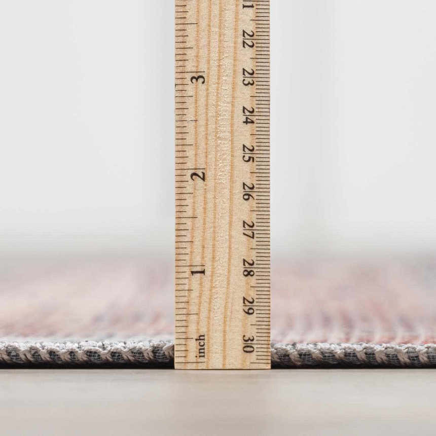 Close-up of the Baltinglass Rust & Blue Washable Area Rug showing the rug's thickness with a ruler. Pile