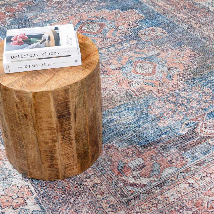 Close-up of the Baltinglass Rust & Blue Washable Area Rug, showcasing its traditional pattern and texture next to a wooden stool. Styleshot