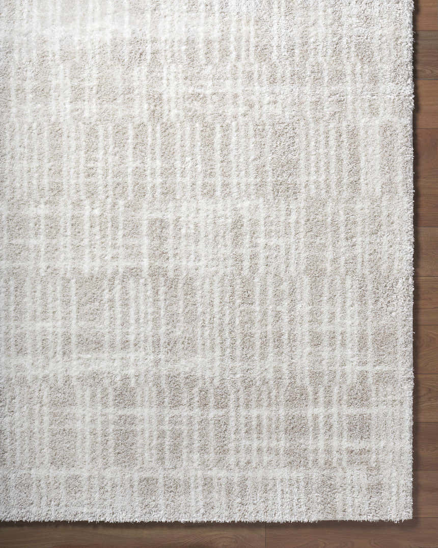 Close-up of the ivory Alamea Area Rug with a subtle geometric shag design on a wood floor. Corner