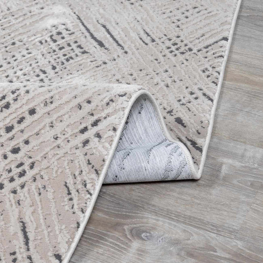Close-up of the Garza Diamond Textured Washable Rug. Beige and gray tones with a modern, abstract pattern. Folded edge detail. Fold