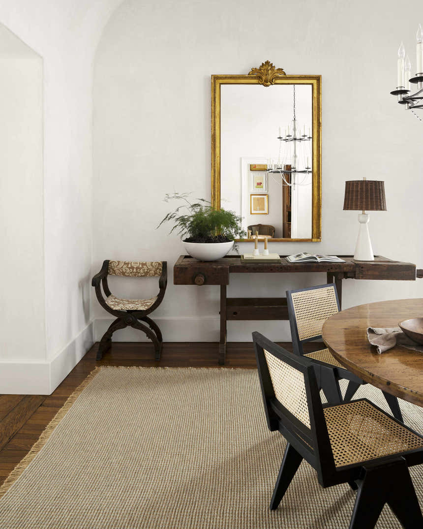 Farmhouse dining room with Kimi Machine Woven Becki Owens rug, wood table, chairs, and gold mirror. Gray, tan, and light brown tones. Styleshot