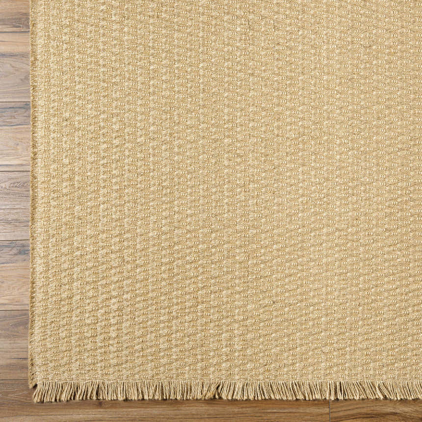 Close-up of the light brown Kimi Becki Owens x LIVABLISS rug showing jute texture and fringe detail on wood floor. Corner