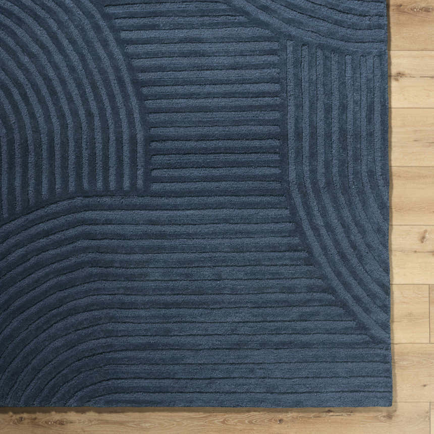 Close up of the hand-tufted Whan Denim Area Rug showing its geometric pattern and textured wool on a wood floor. Corner
