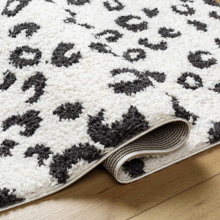 Close-up of the Zhen Black Spots Leopard Rug. Shag rug with a black and white leopard print pattern. Fold
