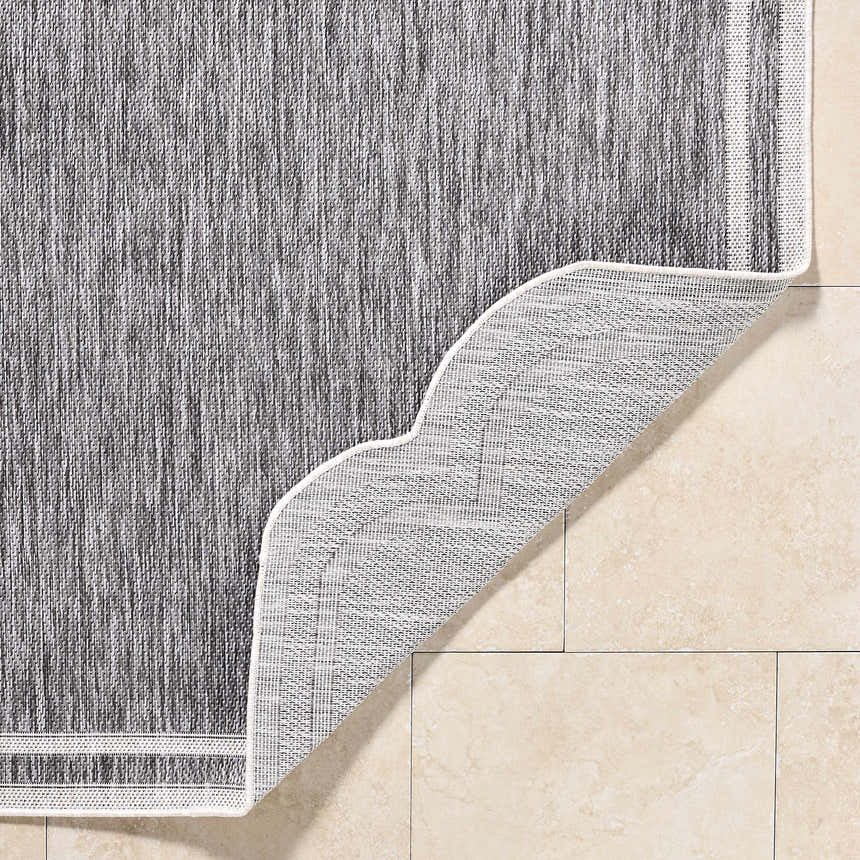 Close-up of Arnola Gray Outdoor Rug showing charcoal and cream fibers, machine woven texture, and polypropylene backing. Fold