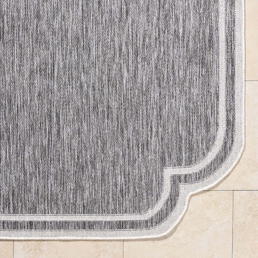 Close-up of Arnola Gray Outdoor Rug showing charcoal and cream fibers and a traditional farmhouse border. Corner