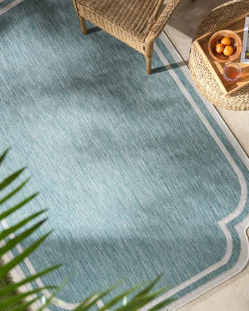 Outdoor patio scene with a light blue Arnola rug, wicker chair, and side table with fruit. Roomscene-Rectangle