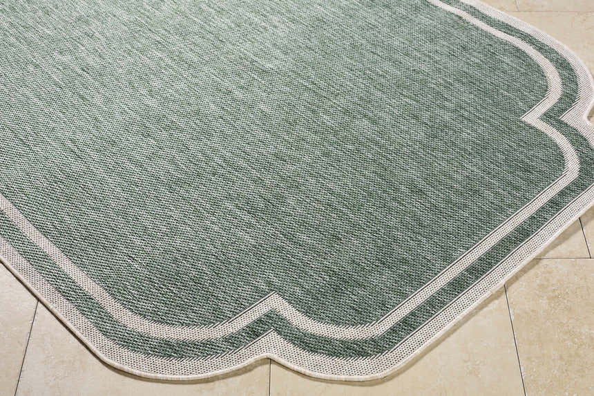 Close-up of Arnola Green Outdoor Rug. Farmhouse style rug with cream border and medium green woven texture. Corner