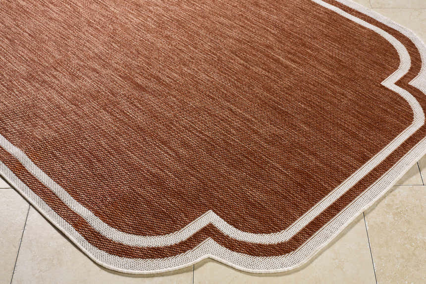 Close-up of Arnola Brown Outdoor Rug showing brown woven texture and cream geometric border on a tile floor. Corner