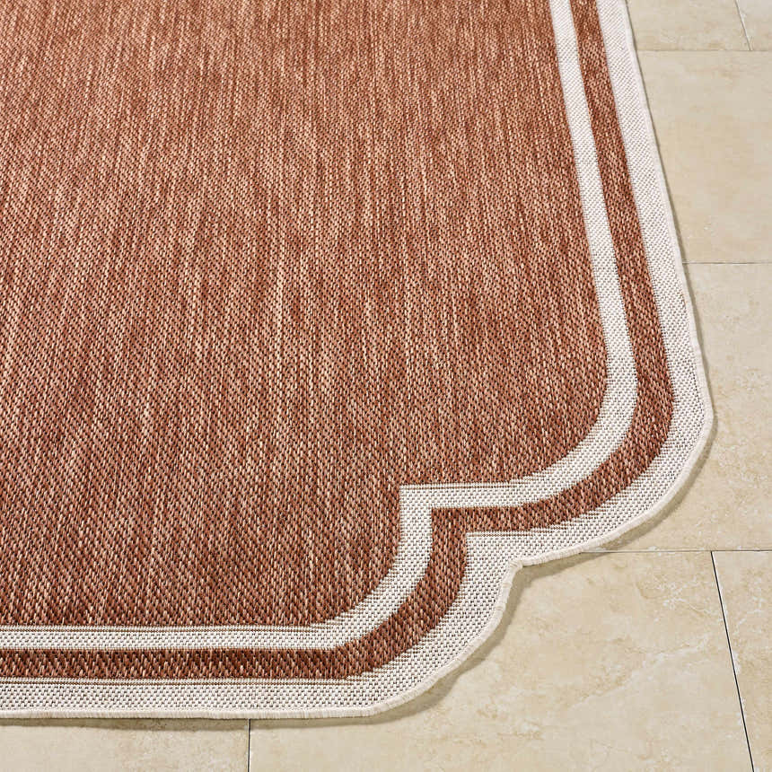 Close-up of Arnola Brown Outdoor Rug showing woven texture, burnt orange color, and cream border on tile floor. Front