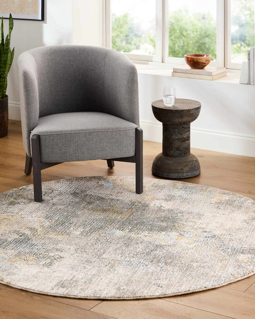 Living room scene with gray chair and round Haydn Rock Pattern Rug in gray, brown, and cream tones. Roomscene-Round
