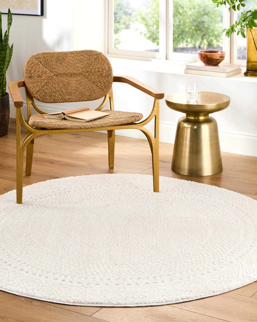 Living room scene with a round Julio Ivory Area Rug, woven chair, and gold side table by a bright window. Roomscene-Round