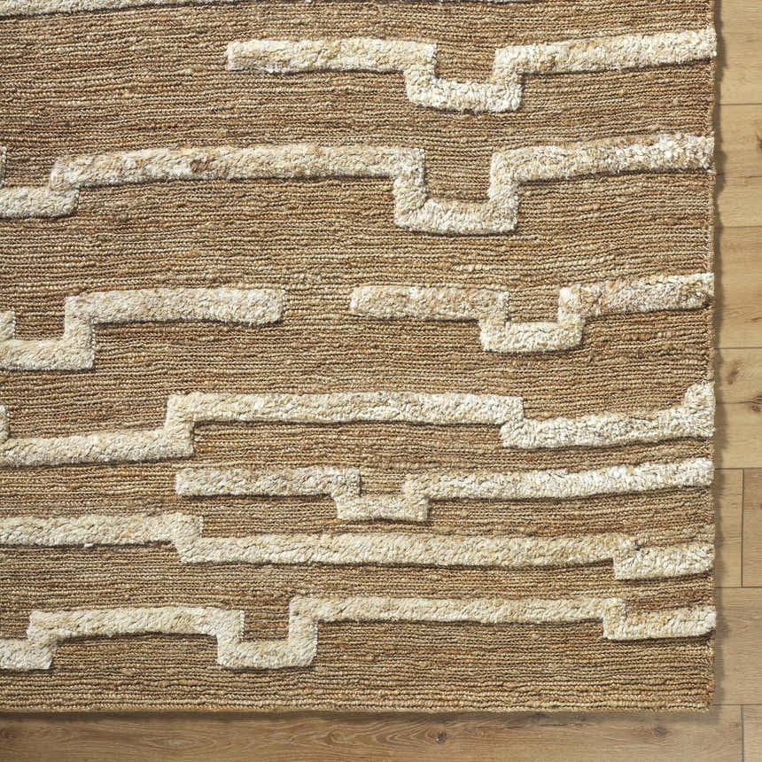 Close-up of the hand-woven Miya Area Rug. Jute rug in beige and tan with a geometric, ivory-colored pattern. Farmhouse style. Corner